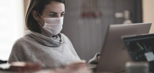 kobieta pracująca zdalnie przed komputerem w masce przeciwbakteryjnej, homeoffice