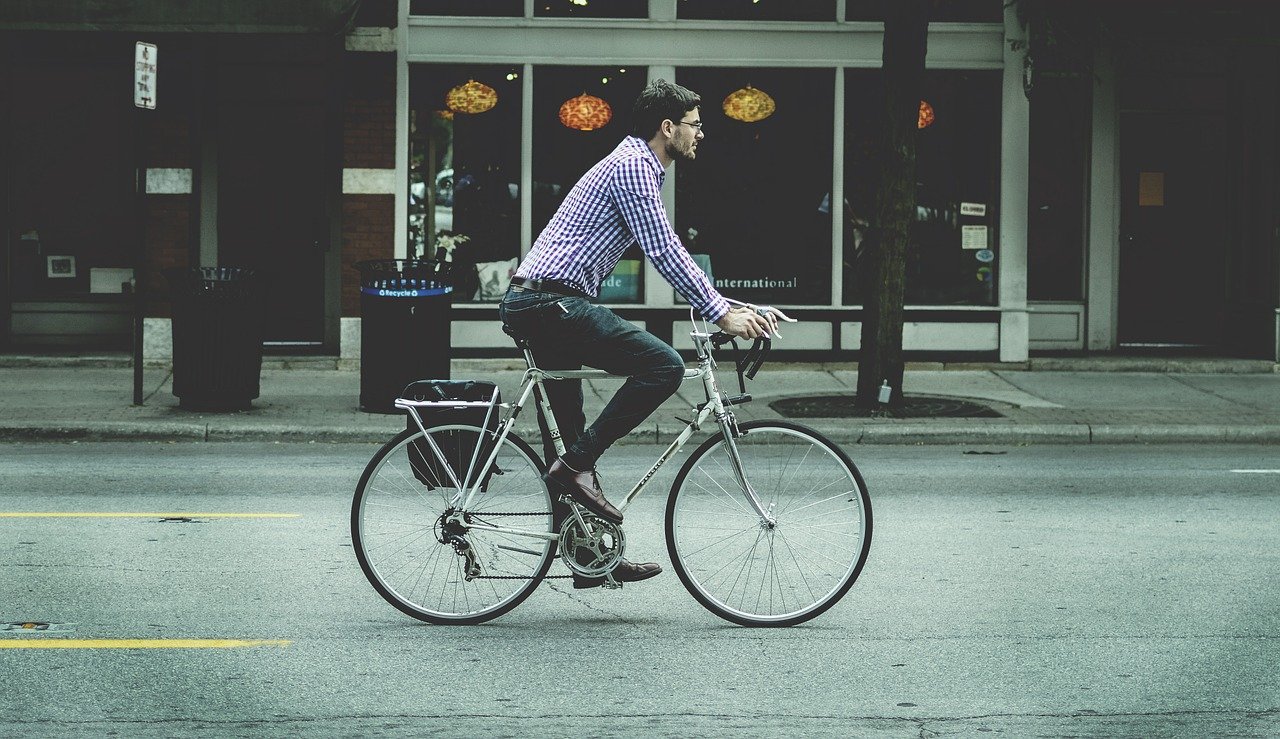 mężczyzna w koszuli i jeansach jadący na rowerze przez miasto