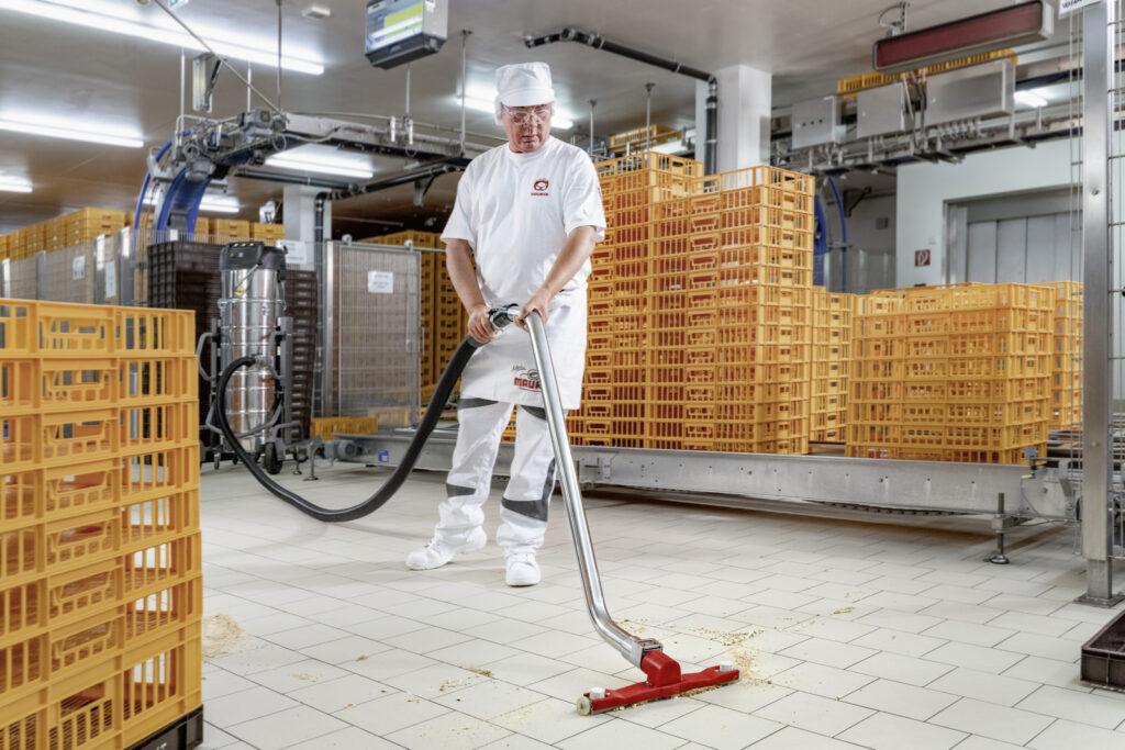 mężczyzna odkurzaczem przemysłowym sprząta resztki po produkcji w piekarni