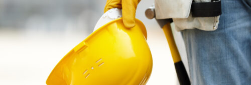 żółty kask i rękawice, odzież BHP, pracownik budowlany trzymający kask ochronny, pas ciesielski, młotek w pasie ciesielskim