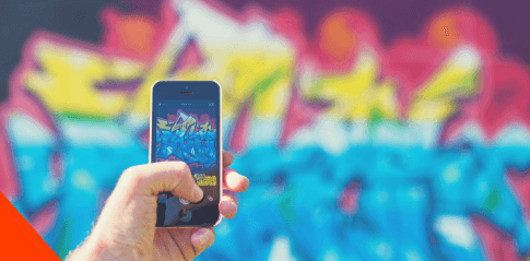 człowiek robiący zdjęcie iphone'm ścianie z kolorowym grafitti.