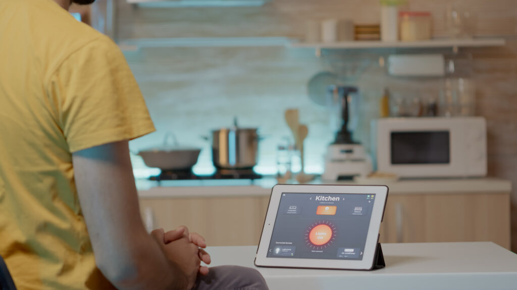 mężczyzna patrzy na tablet, na którym wyświetla się oprogramowanie do sterowania inteligentną kuchniom. Osoba używa tabletu ze smart home aplikacją do sterowania inteligentnym domem.
